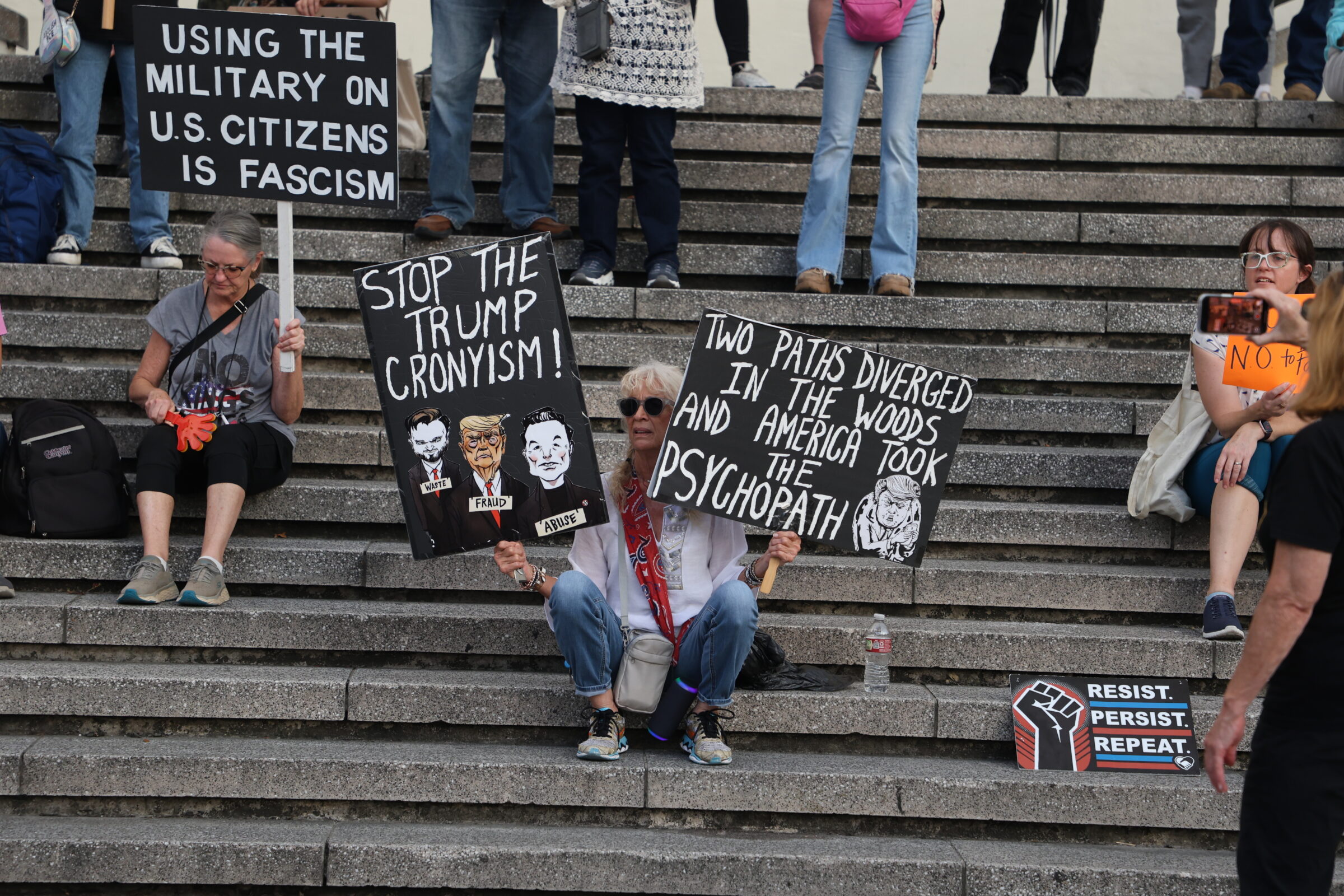 Protestors hold handmade signs protesting President Trump and the use of military force in U.S. cities by deploying National Guard in them on Tuesday, September 16, 2025.